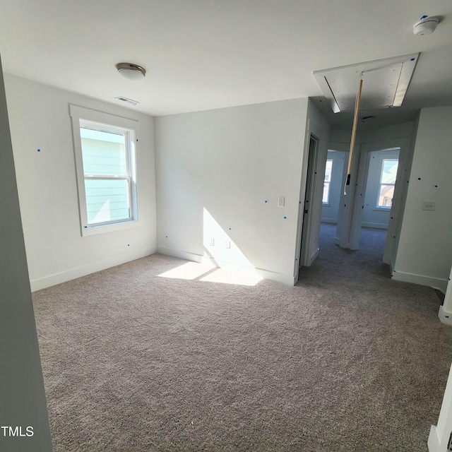 spare room with attic access, carpet flooring, visible vents, and a wealth of natural light