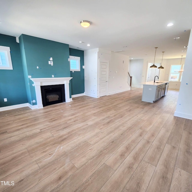 unfurnished living room featuring baseboards, a sink, stairs, a glass covered fireplace, and light wood-type flooring