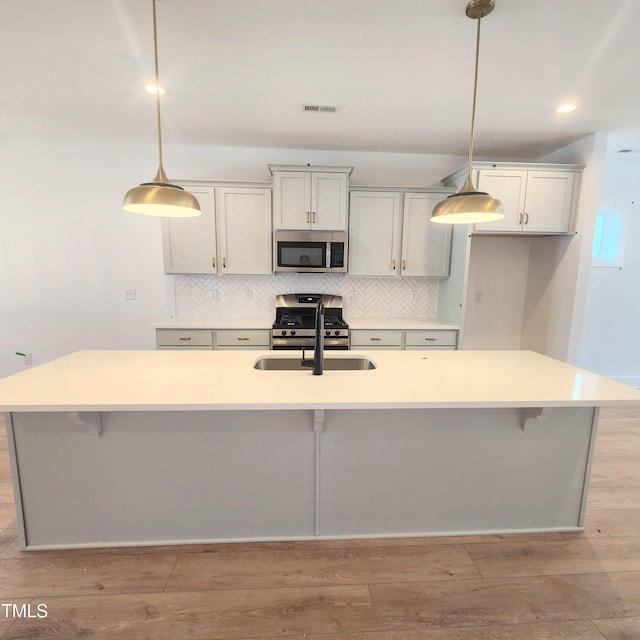 kitchen featuring light wood finished floors, stainless steel microwave, decorative backsplash, and a sink