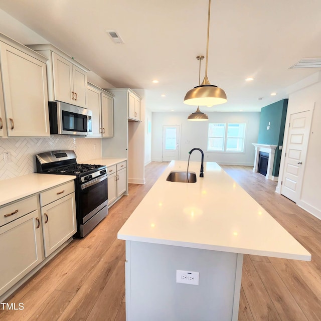 kitchen featuring visible vents, light wood-type flooring, decorative backsplash, appliances with stainless steel finishes, and a sink