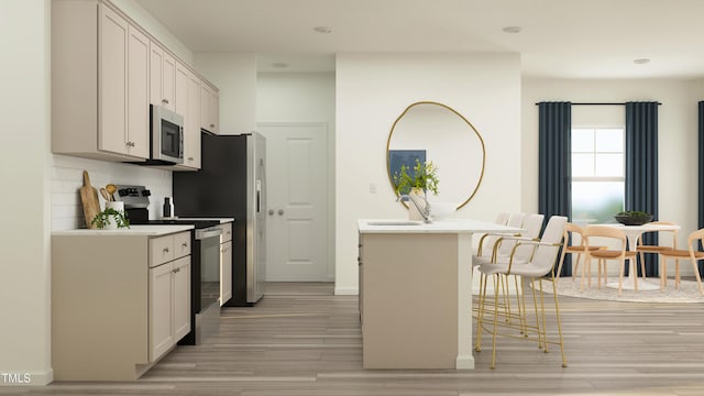 kitchen with a breakfast bar area, light hardwood / wood-style flooring, an island with sink, stainless steel appliances, and white cabinets