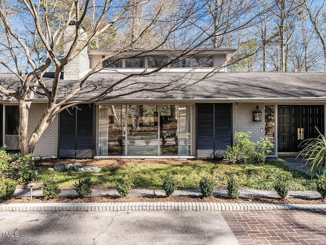 mid-century home featuring roof with shingles and brick siding