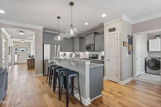 kitchen featuring pendant lighting, gray cabinetry, stainless steel appliances, an island with sink, and washer / dryer