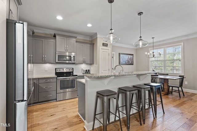 kitchen featuring appliances with stainless steel finishes, a breakfast bar, an island with sink, hanging light fixtures, and light stone counters