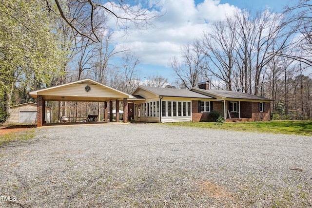 view of front facade with an outbuilding, a chimney, gravel driveway, a carport, and brick siding