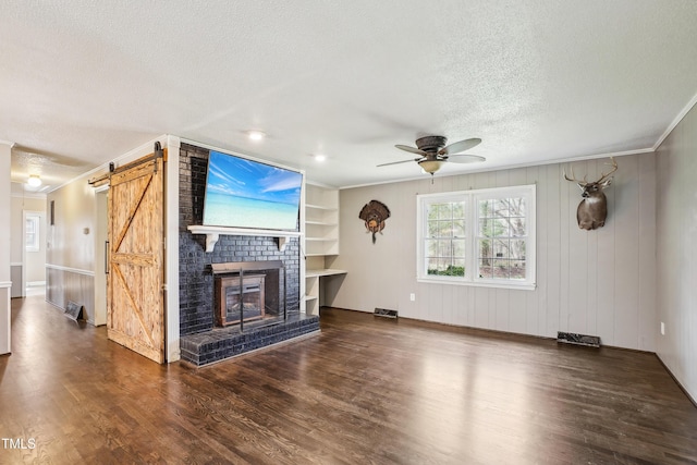 unfurnished living room with crown molding, ceiling fan, a barn door, wood finished floors, and a textured ceiling