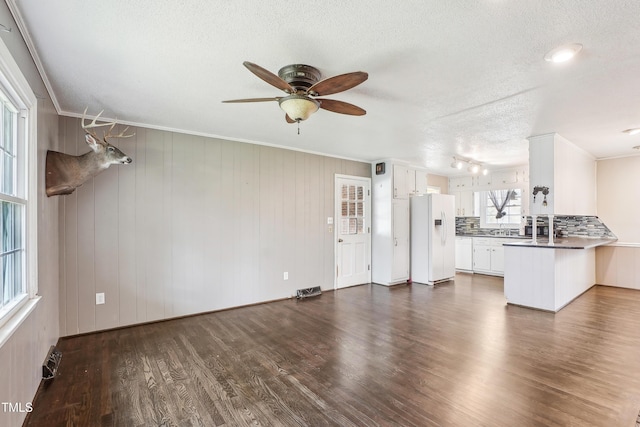 unfurnished living room with a textured ceiling, ceiling fan, dark wood-style flooring, and crown molding