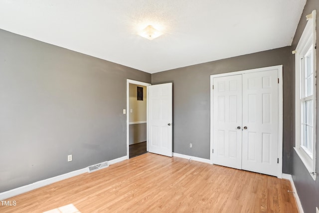 unfurnished bedroom featuring baseboards, visible vents, a closet, and light wood-type flooring