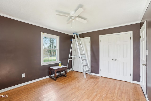 unfurnished bedroom with crown molding, baseboards, light wood-type flooring, and two closets