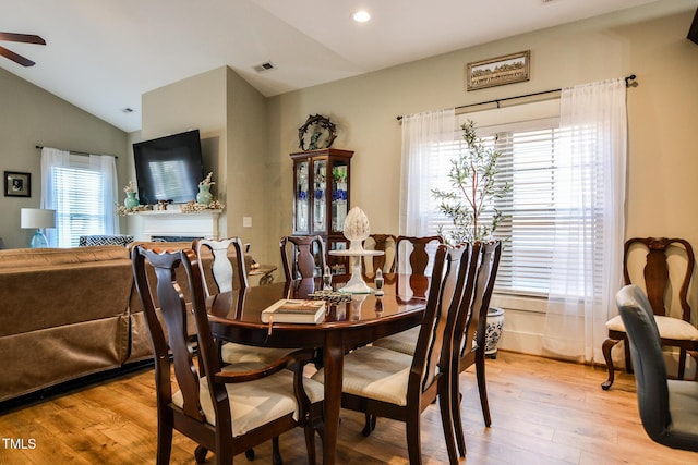 dining area with lofted ceiling, light wood finished floors, a fireplace, and visible vents