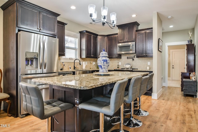 kitchen featuring dark brown cabinetry, a sink, appliances with stainless steel finishes, light stone countertops, and tasteful backsplash