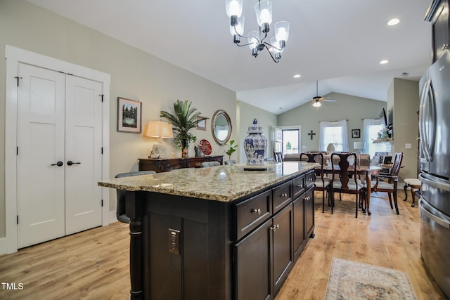 kitchen featuring light stone counters, pendant lighting, light wood finished floors, freestanding refrigerator, and vaulted ceiling