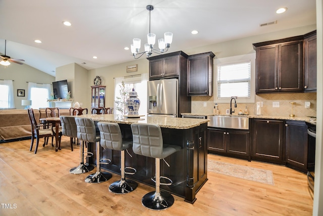 kitchen with a breakfast bar, a kitchen island, a sink, open floor plan, and stainless steel refrigerator with ice dispenser