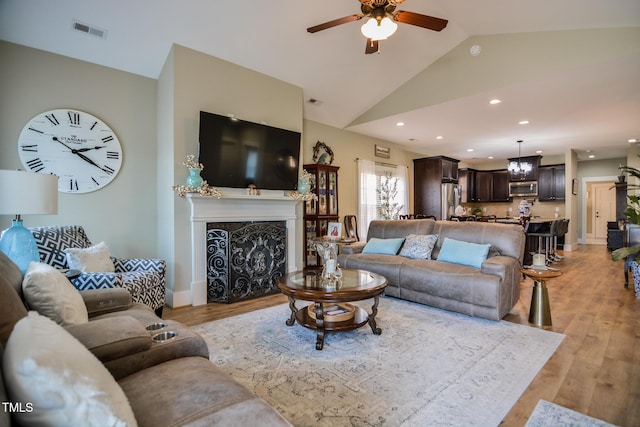 living area featuring light wood finished floors, visible vents, lofted ceiling, ceiling fan, and a fireplace