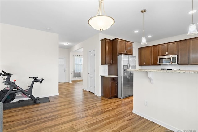 kitchen featuring a kitchen bar, hanging light fixtures, light wood-type flooring, appliances with stainless steel finishes, and light stone countertops