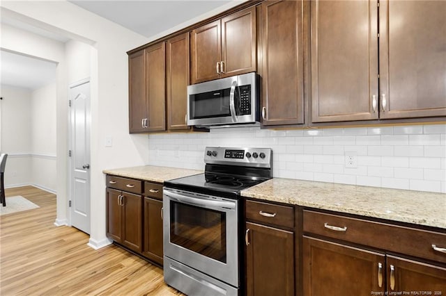 kitchen featuring appliances with stainless steel finishes, dark brown cabinetry, light stone countertops, decorative backsplash, and light wood-type flooring