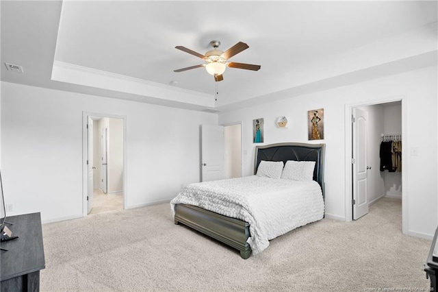 carpeted bedroom with ceiling fan, a walk in closet, and a raised ceiling