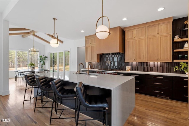 kitchen featuring sink, a breakfast bar area, tasteful backsplash, wood-type flooring, and a kitchen island with sink