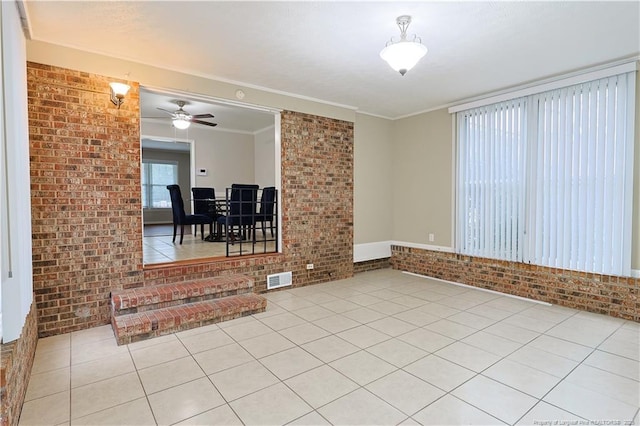 tiled empty room featuring crown molding, ceiling fan, and brick wall