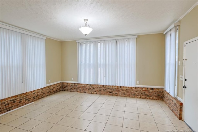 tiled spare room featuring ornamental molding, brick wall, and a textured ceiling