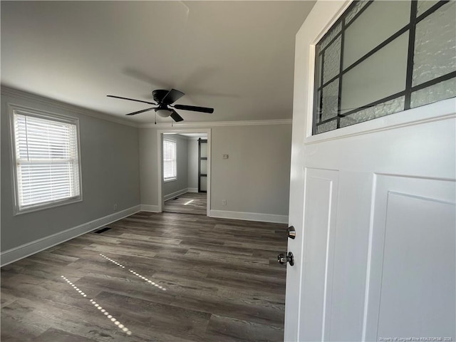 unfurnished room with visible vents, a ceiling fan, dark wood-style floors, crown molding, and baseboards