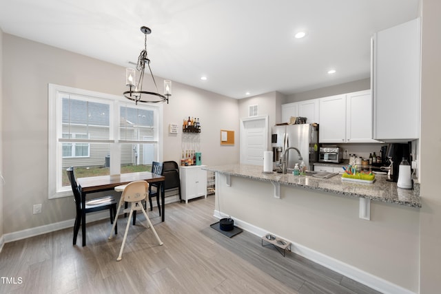 kitchen featuring white cabinetry, light stone counters, decorative light fixtures, stainless steel fridge with ice dispenser, and kitchen peninsula