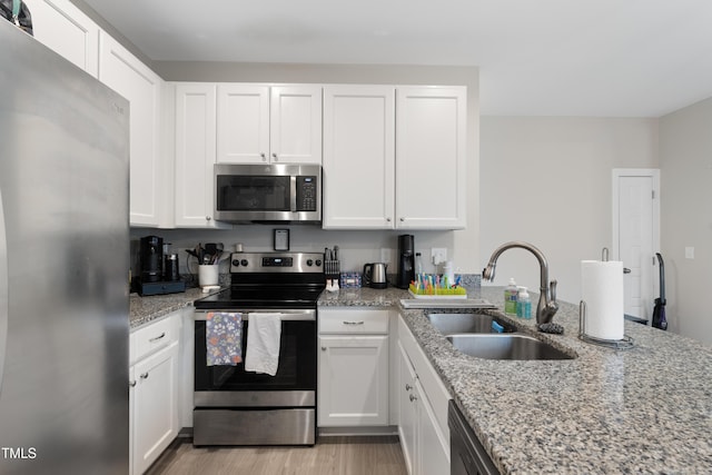 kitchen with stainless steel appliances, light stone countertops, sink, and white cabinets