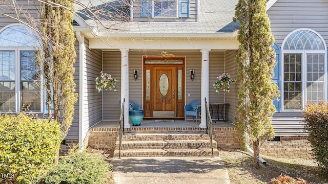 view of exterior entry featuring covered porch and roof with shingles