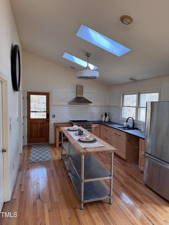 kitchen with appliances with stainless steel finishes, vaulted ceiling with skylight, sink, and wall chimney range hood