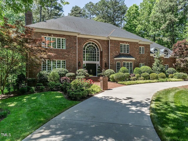 view of front of home with brick siding, a front lawn, and a chimney