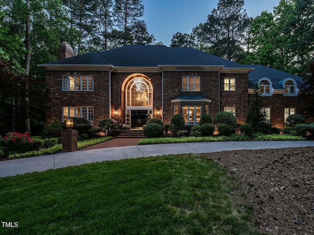 view of front of house with a front yard, a chimney, concrete driveway, and brick siding