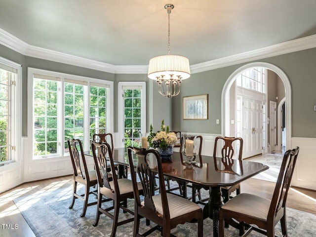 dining room featuring a wainscoted wall, a notable chandelier, arched walkways, and crown molding