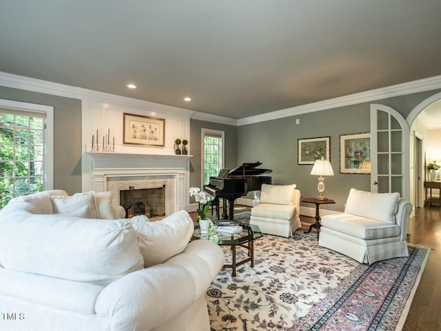 living room with arched walkways, recessed lighting, a tiled fireplace, ornamental molding, and wood finished floors