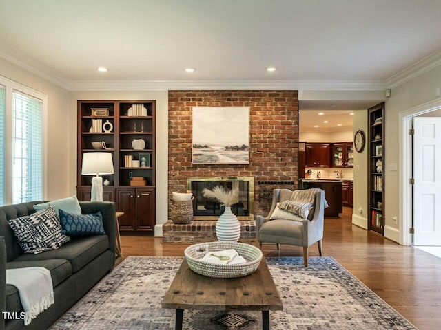 living room with built in features, recessed lighting, ornamental molding, a brick fireplace, and wood finished floors