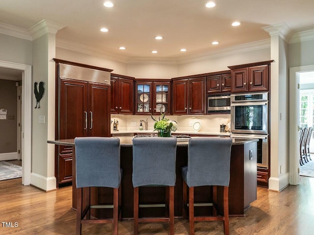 kitchen with a kitchen island, appliances with stainless steel finishes, wood finished floors, and ornamental molding