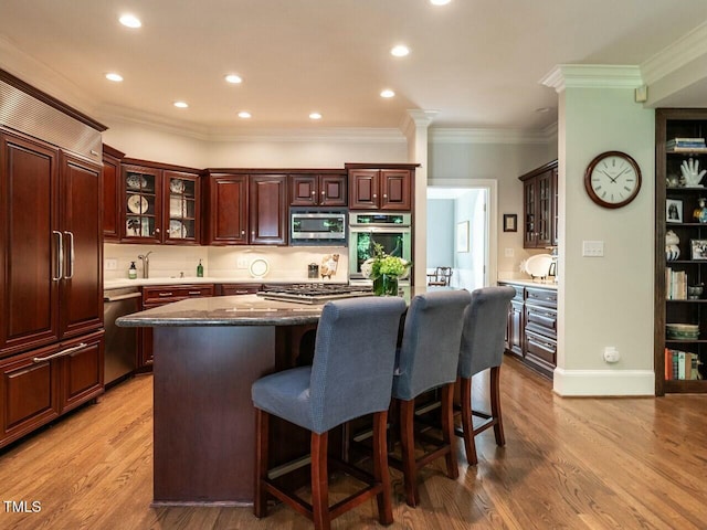 kitchen featuring a breakfast bar, a kitchen island, appliances with stainless steel finishes, light wood finished floors, and crown molding