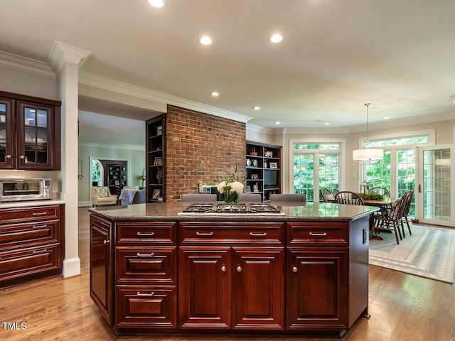 kitchen with reddish brown cabinets, ornamental molding, wood finished floors, stainless steel gas stovetop, and pendant lighting