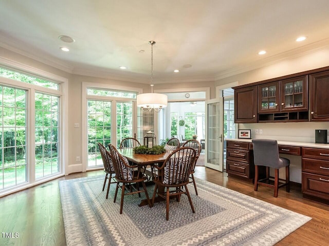 dining space featuring ornamental molding, a healthy amount of sunlight, built in desk, and wood finished floors