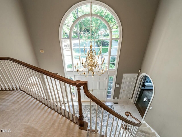 stairs featuring a chandelier, carpet floors, and a high ceiling