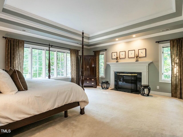 carpeted bedroom with a fireplace with flush hearth, multiple windows, a tray ceiling, and crown molding