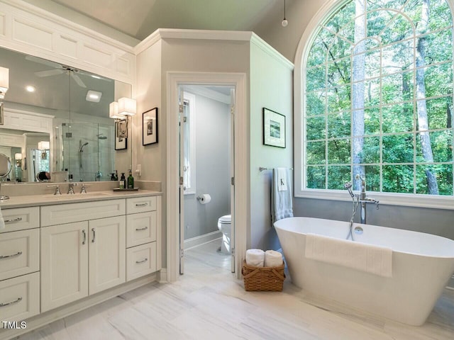 full bath with toilet, a stall shower, ceiling fan, vanity, and a freestanding tub