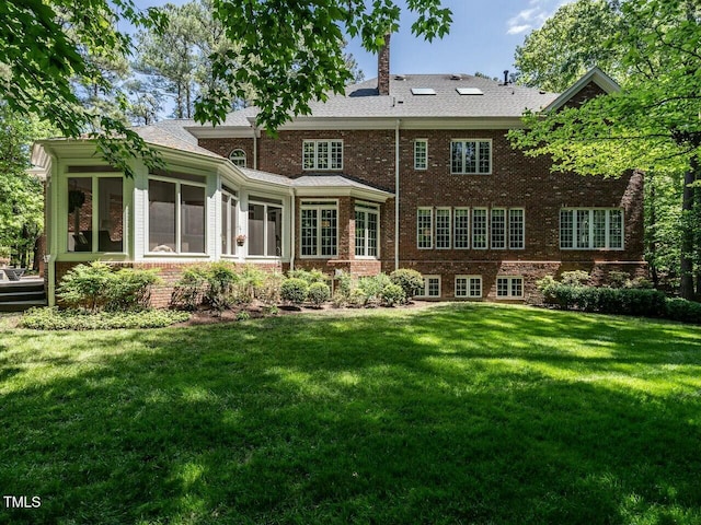 rear view of property featuring a sunroom, brick siding, and a yard