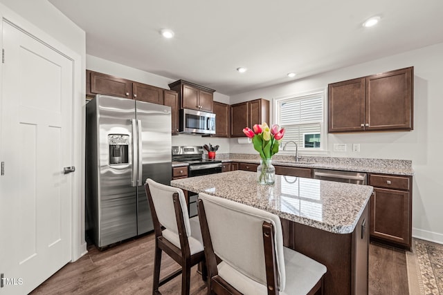 kitchen with a breakfast bar, a sink, appliances with stainless steel finishes, a center island, and dark wood-style floors