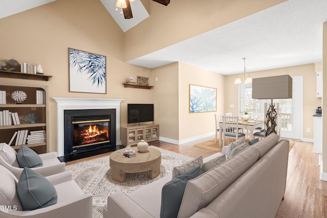 living room featuring ceiling fan with notable chandelier, light hardwood / wood-style flooring, and vaulted ceiling