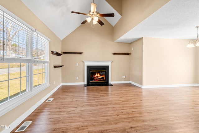 unfurnished living room featuring high vaulted ceiling, ceiling fan with notable chandelier, and light hardwood / wood-style floors