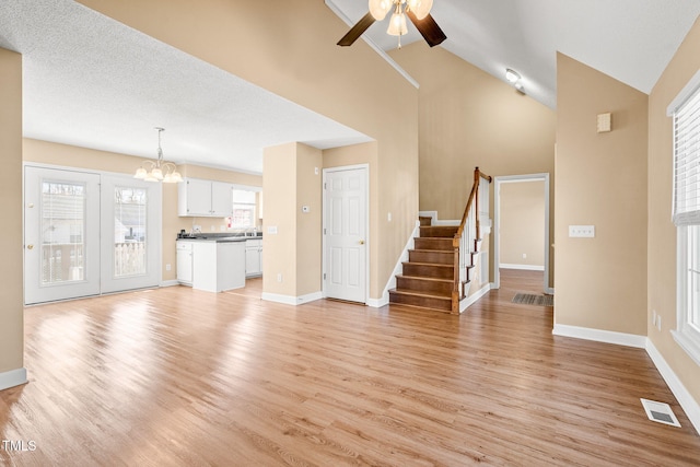 unfurnished living room with high vaulted ceiling, sink, ceiling fan with notable chandelier, and light wood-type flooring