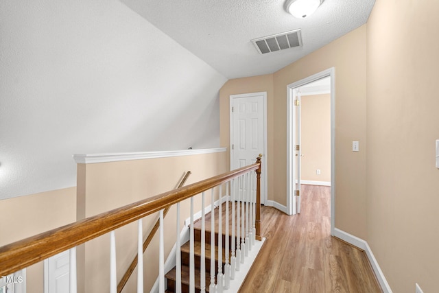 hall with lofted ceiling, a textured ceiling, and light hardwood / wood-style flooring