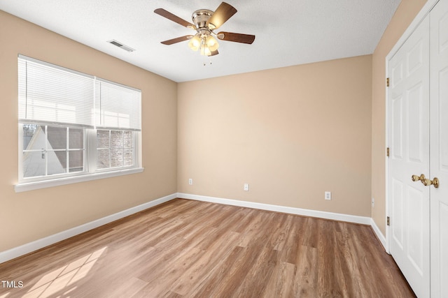 unfurnished bedroom featuring ceiling fan, a closet, a textured ceiling, and light wood-type flooring