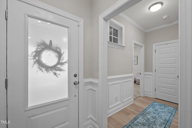 foyer entrance with light wood-style floors, ornamental molding, a decorative wall, and a wainscoted wall