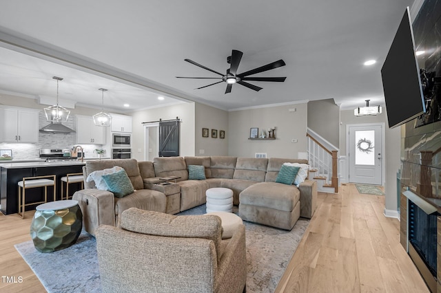 living area featuring a barn door, ceiling fan, stairway, crown molding, and light wood-style floors